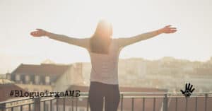 De costas, mulher de cabelos compridos está com os dois braços abertos, perpendiculares ao corpo, sua frente virada para o por do sol. No canto inferior esquerdo "#BlogueirxsAME".