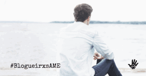 Homem de cabelos curtos, lisos e escuros,sentado de costas, vestido em uma camisa branca de mangas compridas, calça jeans. À sua frente, desfocado, o mar. No canto inferior esquerdo, "#BlogueirxsAME", no canto inferior direito o desenho, em preto, de uma mão com um coração no centro e escrito, embaixo do coração, "AME".