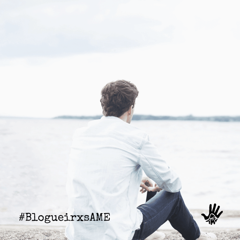 Homem de cabelos curtos, lisos e escuros,sentado de costas, vestido em uma camisa branca de mangas compridas, calça jeans. À sua frente, desfocado, o mar. No canto inferior esquerdo, "#BlogueirxsAME", no canto inferior direito o desenho, em preto, de uma mão com um coração no centro e escrito, embaixo do coração, "AME".