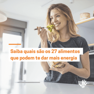 Mulher de cabelos lisos e loiros segura, com a mão esquerda, uma vasilha transparente com salada dentro. Com a mão direita, ela segura um garfo com folhas verdes levantado em frente à sua boca, que está aberta em um sorriso. Ela veste camiseta de mangas curtas cinza. Texto com fundo branco e letras laranjas, centralizado na imagem, lê "Saiba quais são os 27 alimentos que podem te dar mais energia"